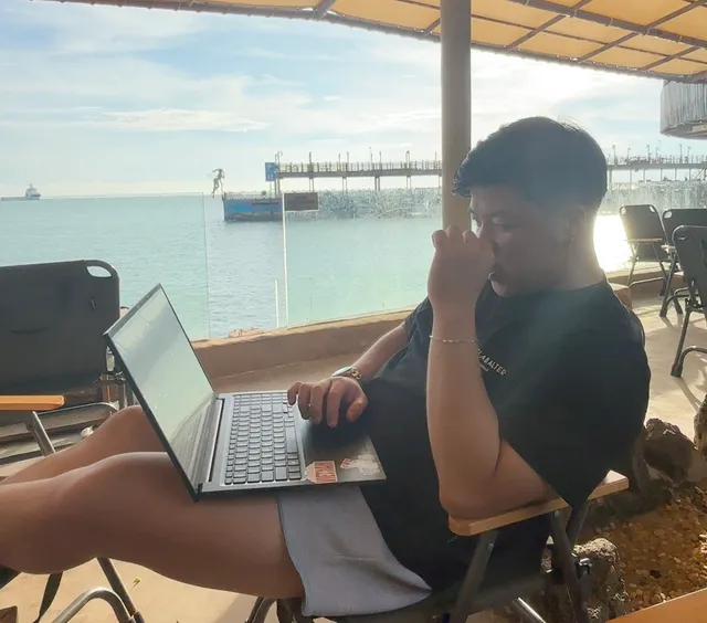 Duy làm việc trên laptop bên bờ biển